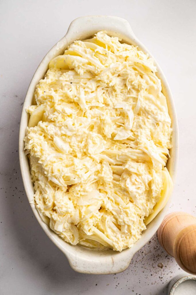 A creamy cheese and onion mixture is spread over layered potato slices in a baking dish.
