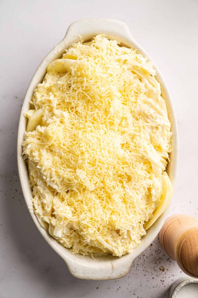 Shredded cheese tops the assembled potato gratin in a baking dish, ready to go into the oven.