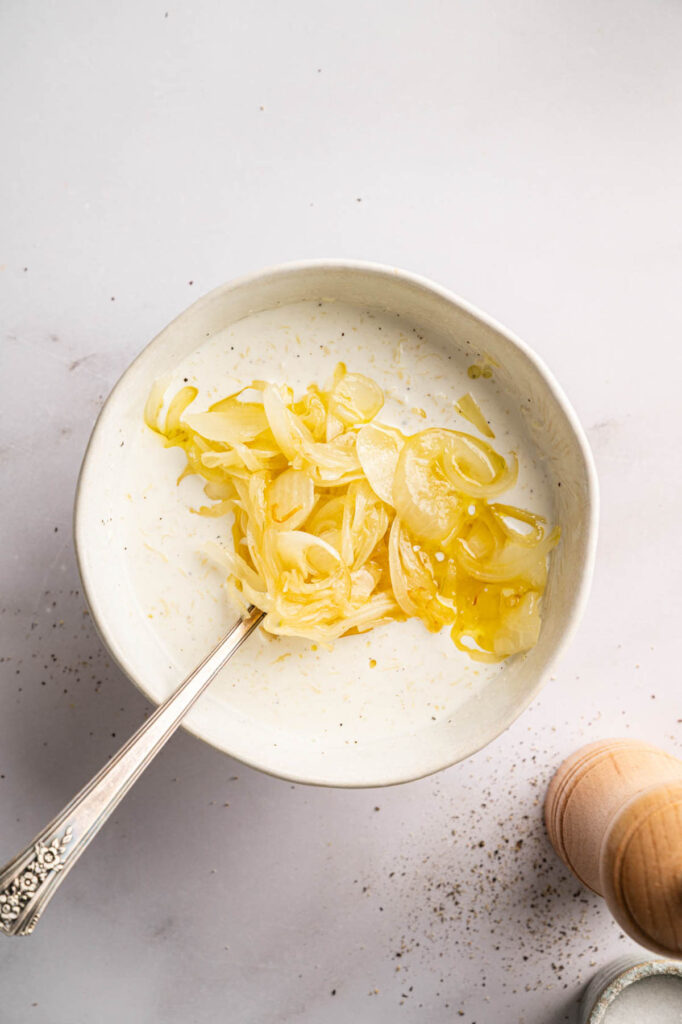 Caramelized onions are stirred into a bowl of cream, ready to be mixed with grated cheese.