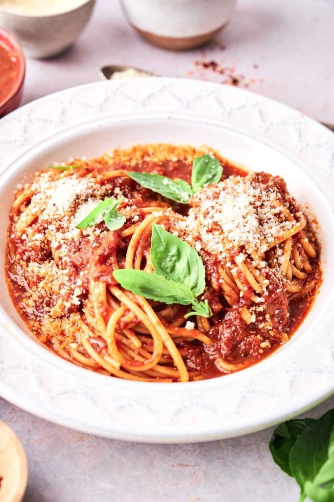 A plate of Spaghetti Marinara topped with tomato sauce, grated cheese, and fresh basil leaves.