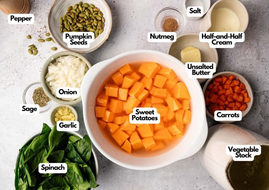 A variety of labeled ingredients for Sweet Potato Soup, including sweet potatoes, spinach, onion, garlic, sage, carrots, pumpkin seeds, seasonings, cream, butter, and vegetable stock.