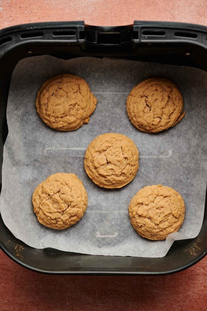 Five round Air Fryer Biscoff Sandwich Cookies rest on parchment paper inside an air fryer basket.
