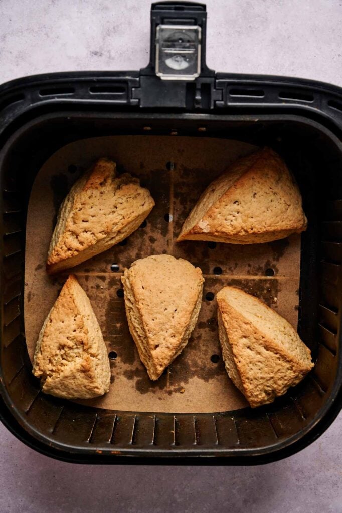 Four golden-brown Air Fryer Scones are arranged on parchment paper inside an air fryer basket.