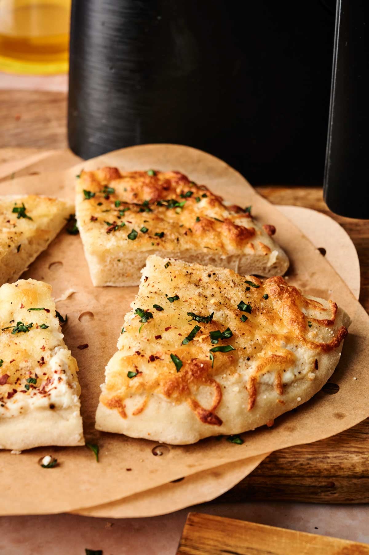 Three slices of cheesy focaccia bread with herbs on parchment paper, placed on a wooden board&mdash;perfect as a side for your favorite Air Fryer White Pizza.