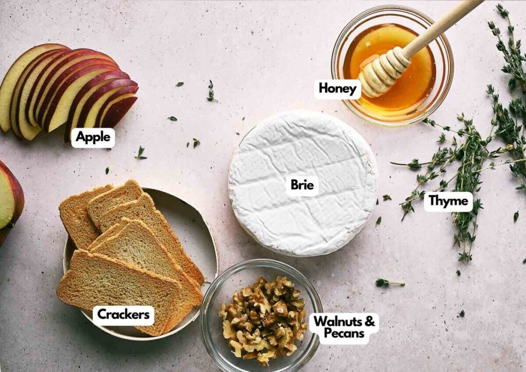 Top-down view of sliced apple, crackers, Baked Brie cheese, honey with dipper, thyme sprigs, and a bowl of mixed walnuts and pecans, each labeled.