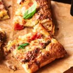 A close-up of rectangular slices of Air Fryer Pesto Pizza, with puff pastry topped with melted cheese, tomato, herbs, and fresh basil on parchment paper.