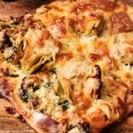 Close-up of a delicious Air Fryer Spinach Pizza, topped with artichoke hearts and melted cheese, served on a wooden surface.