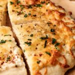 A close-up of sliced cheesy garlic bread topped with herbs and seasoning on parchment paper, reminiscent of Air Fryer White Pizza flavors.