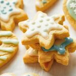 A close-up of Christmas Sugar Cookies stacked and decorated with white and pastel-colored icing on a white surface.
