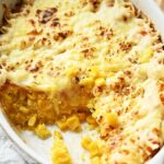 Corn Casserole baked to perfection, topped with melted cheese, and partially served to reveal layers of corn and other ingredients inside a white oval dish.