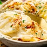 A baked dish of scalloped potatoes topped with melted cheese and garnished with chopped parsley, this Air Fryer Potatoes Au Gratin is served hot with a golden spatula for the perfect crispy finish.