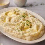 A plate of Southern Mash Potato topped with butter, chopped parsley, and black pepper, served on a white dish.