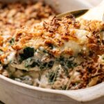 A close-up of a creamy Spinach Casserole with a crispy breadcrumb topping being lifted from a baking dish.