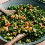 A vibrant bowl of tabbouleh salad, featuring chopped parsley, tomatoes, cucumber, and bulgur, is mixed to perfection with wooden serving spoons. Tabbouleh’s fresh flavors make it a delicious Mediterranean favorite.