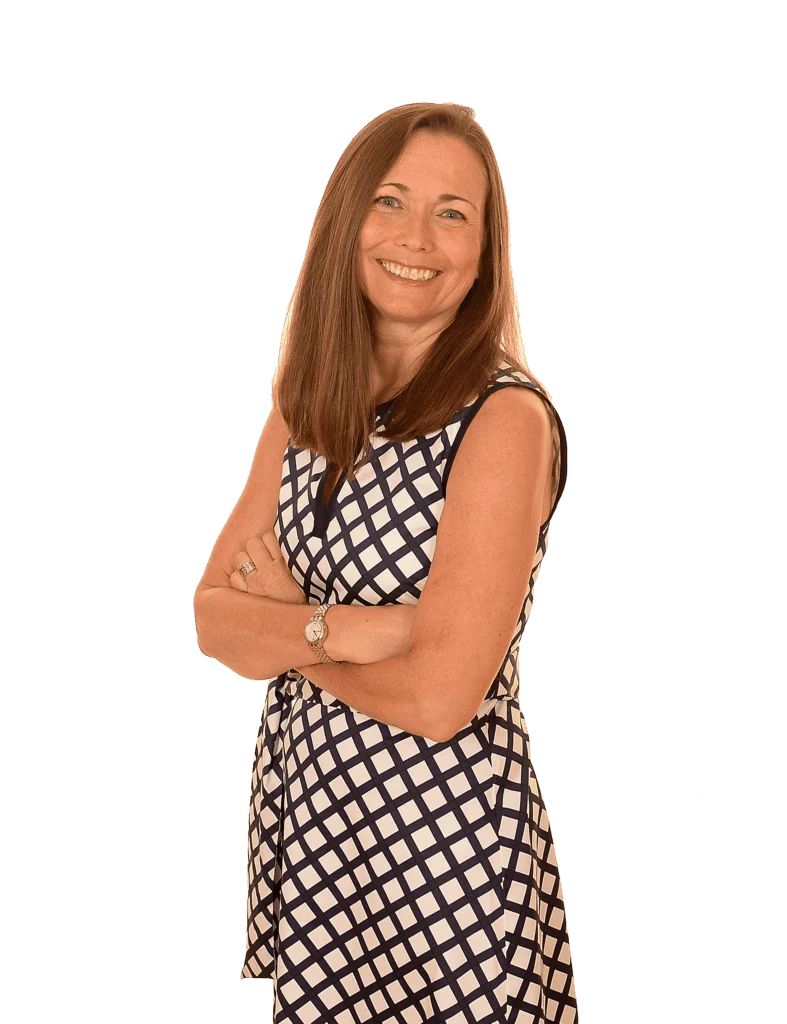 Woman with long brown hair, wearing a sleeveless, black and white checkered dress, standing with arms crossed and smiling at the camera.