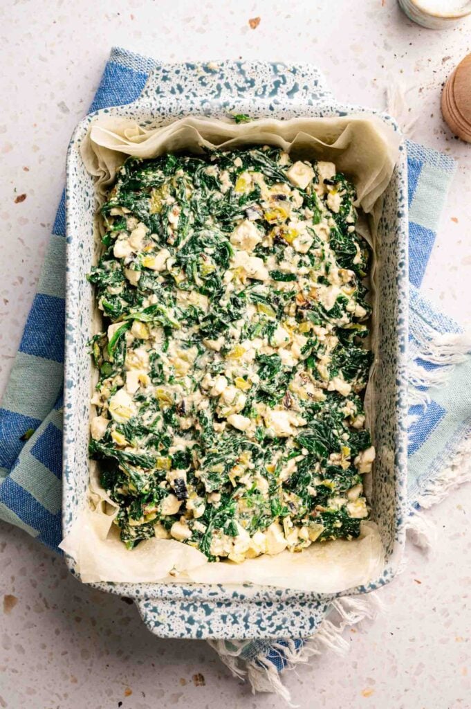 The spinach and feta filling is spread evenly over the phyllo base in a baking dish.