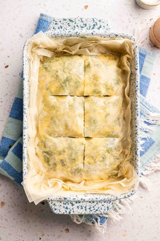 The top layer of phyllo is brushed with olive oil and scored into squares before baking.