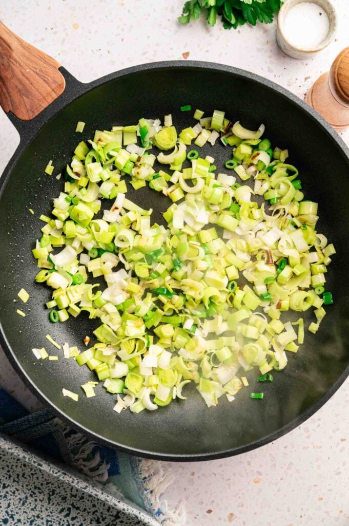 Chopped leeks and green onions cook down in a skillet until softened, the aromatic base for spanakopita.