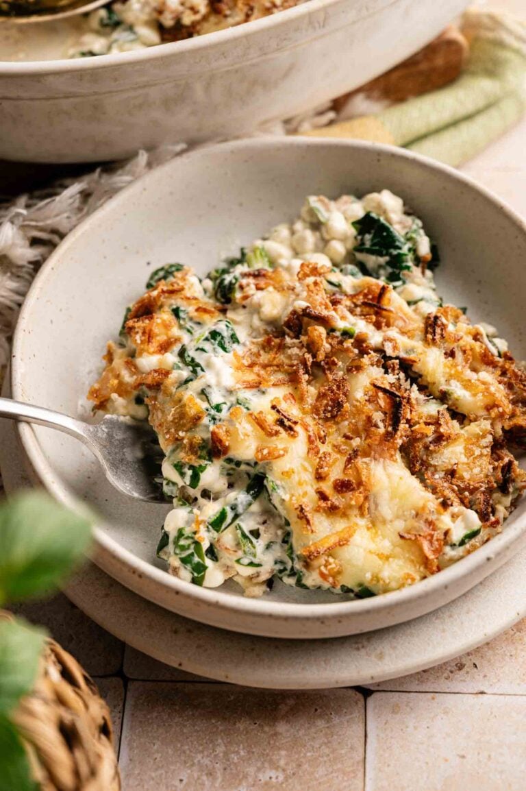 A bowl of creamy Spinach Casserole with cheese, topped with crispy fried onions and served with a fork.