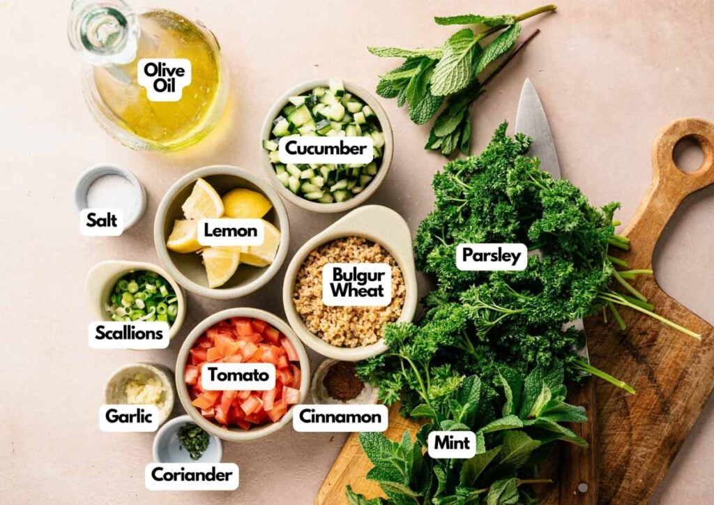 A vibrant tabbouleh spread featuring labeled ingredients like bulgur wheat, parsley, mint, cucumber, tomato, scallions, garlic, lemon, olive oil, cinnamon, coriander, and salt.