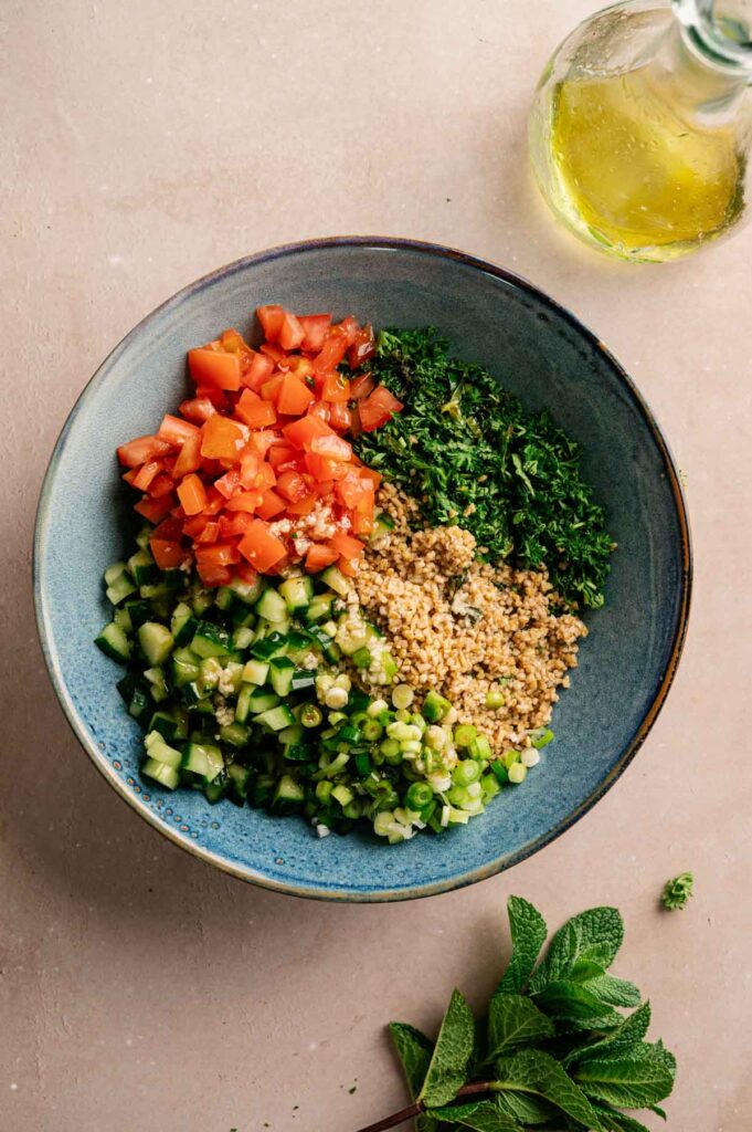 Diced tomato, cucumber, scallions, bulgur, and chopped parsley sit in sections in a blue bowl, ready to be mixed.