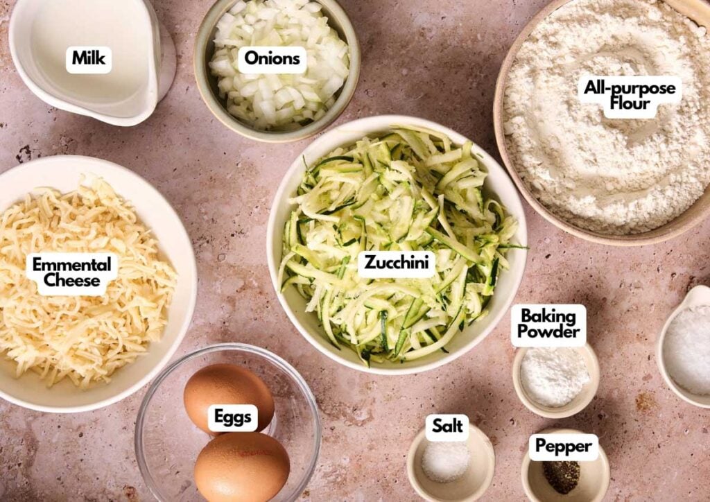 Bowls of grated Emmental cheese, shredded zucchini, chopped onions, and other fresh ingredients are arranged on a countertop—perfect for making delicious Air Fryer Zucchini Muffins.