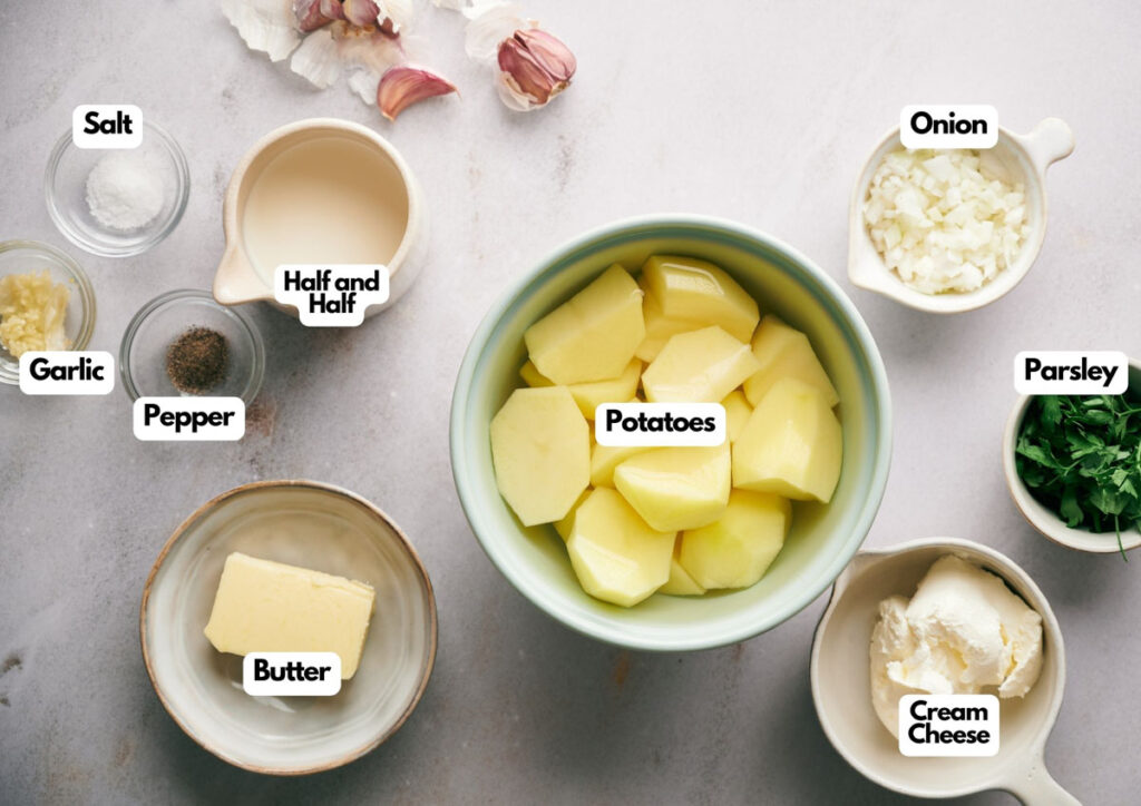 Labeled ingredients for Southern Mash Potato, including peeled potatoes, chopped onion, parsley, cream cheese, butter, garlic, pepper, salt, and half and half are arranged on a counter.