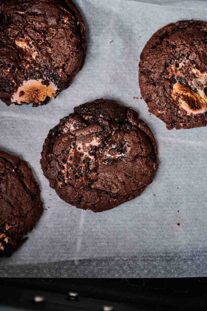 Four Air Fryer Marshmallow Swirl Cookies with visible chunks of marshmallow are placed on a sheet of parchment paper.