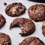 Several Air Fryer Marshmallow Swirl Cookies are arranged on white parchment paper, with one cookie showing a bite taken out of it.