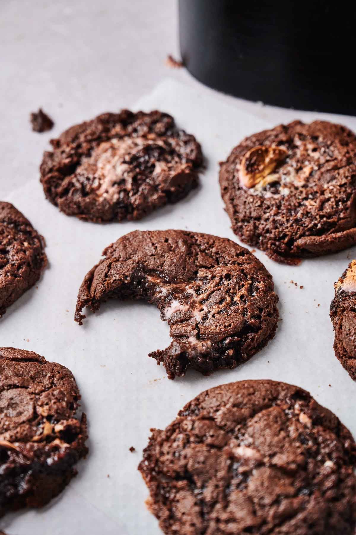 Several Air Fryer Marshmallow Swirl Cookies are arranged on white parchment paper, with one cookie showing a bite taken out of it.