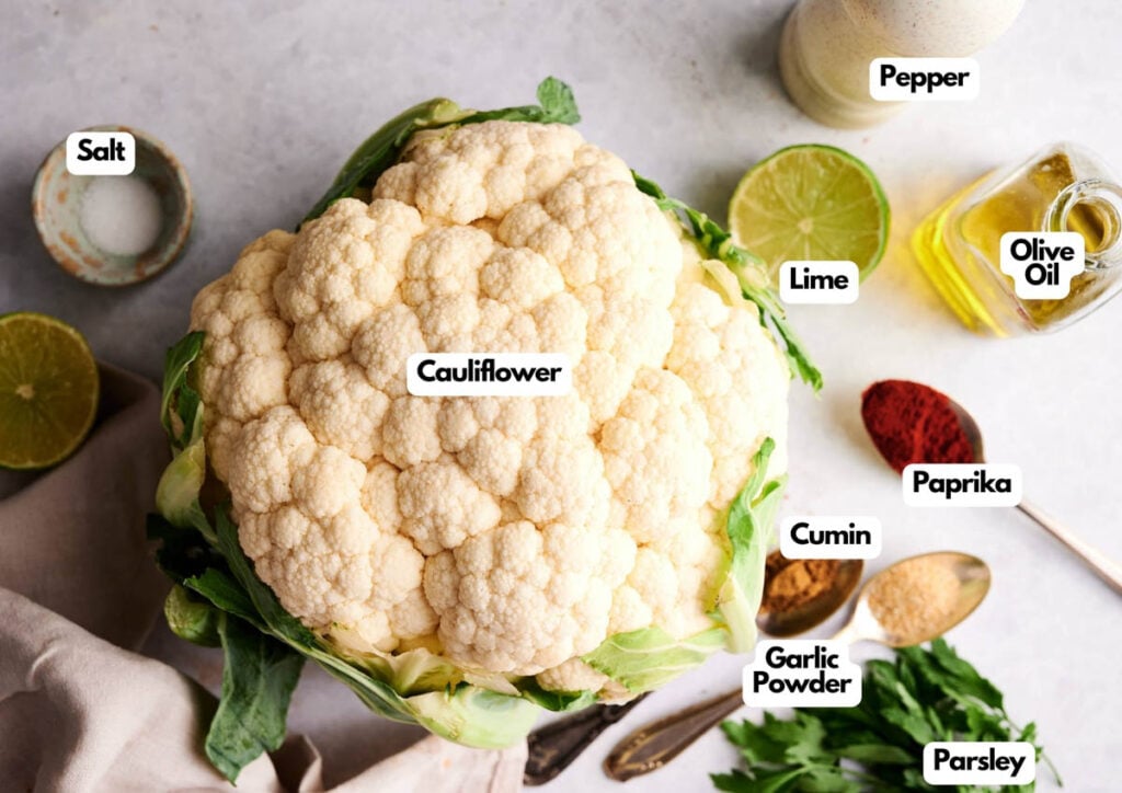 A head of cauliflower surrounded by labeled ingredients: salt, pepper, olive oil, lime, paprika, cumin, garlic powder, and parsley&mdash;perfect for making flavorful Air Fryer Roasted Whole Cauliflower.