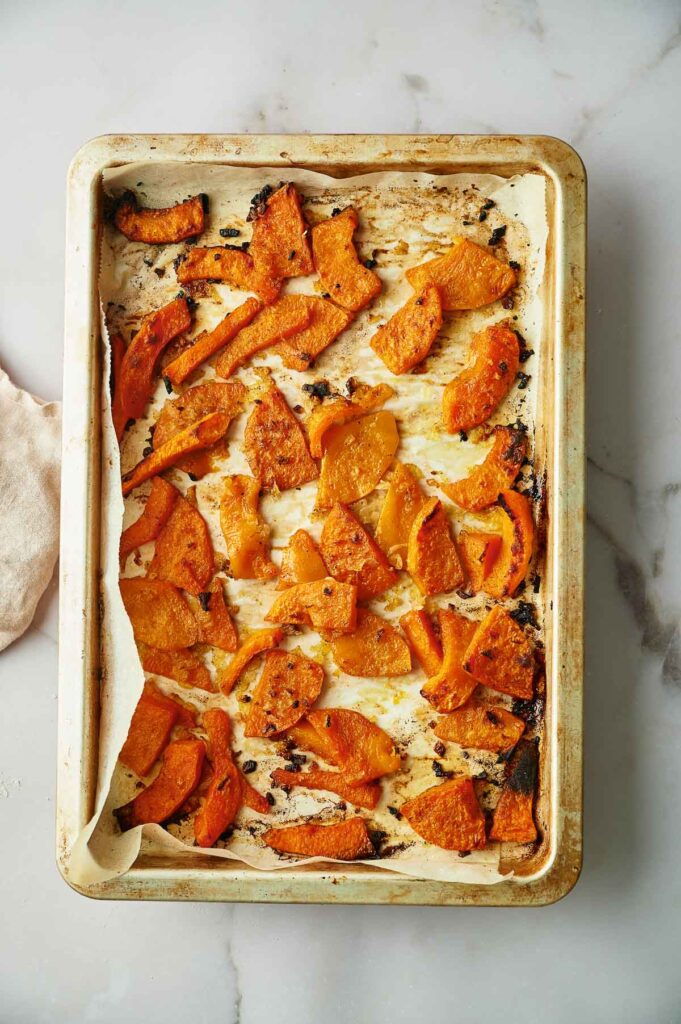 Baking tray lined with parchment paper holding roasted, sliced pieces of butternut squash on a marble surface&mdash;perfect for adding to your next Yellow Squash Casserole.