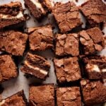 Squares of Air Fryer Cream Cheese Brownies, with a visible cream cheese layer in the middle, are arranged on parchment paper.