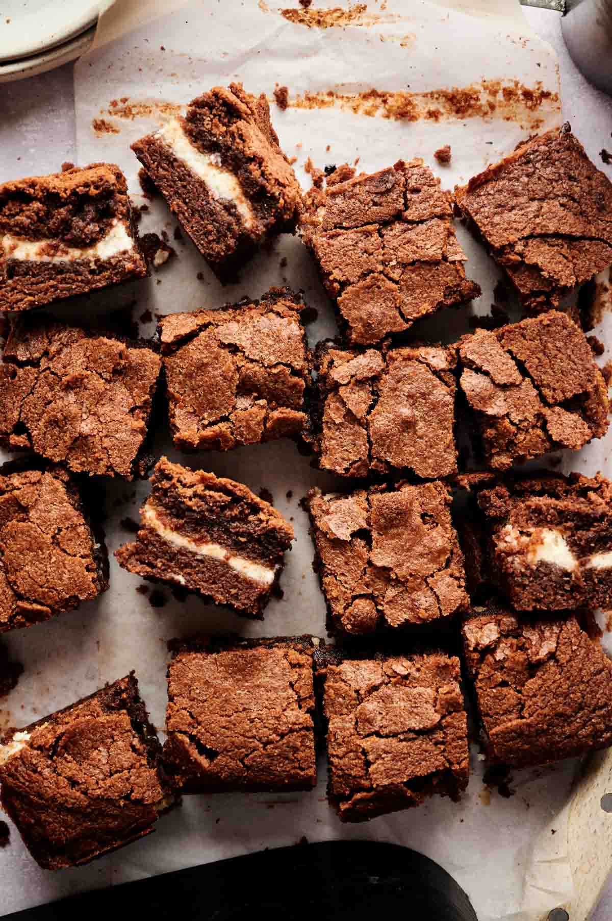 Squares of Air Fryer Cream Cheese Brownies, with a visible cream cheese layer in the middle, are arranged on parchment paper.