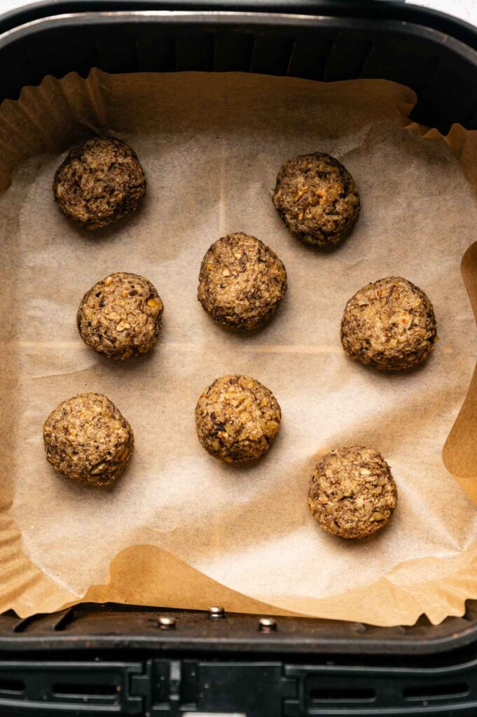 Eight uncooked Air Fryer Vegetarian Meatballs are arranged on parchment paper inside an air fryer basket.
