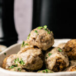 A close-up of a bowl filled with air fryer vegetarian meatballs covered in creamy sauce and garnished with chopped herbs.