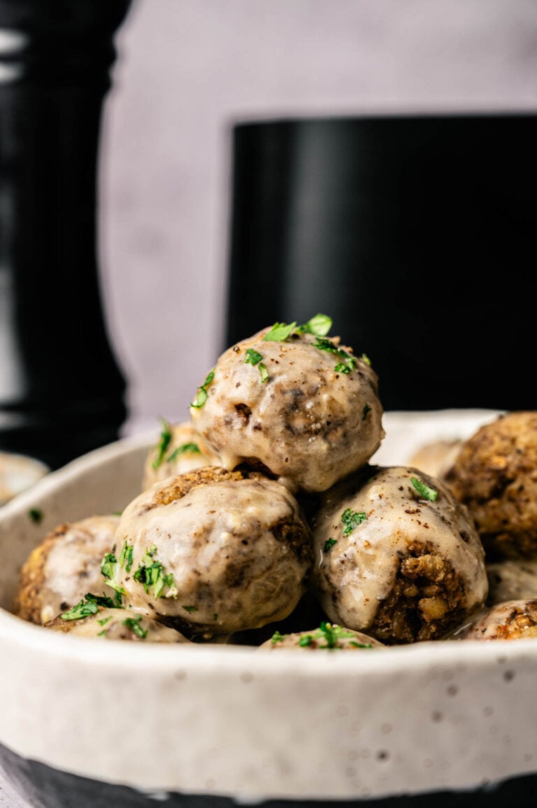 A close-up of a bowl filled with air fryer vegetarian meatballs covered in creamy sauce and garnished with chopped herbs.