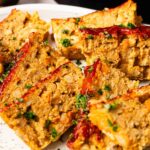 Several slices of Air Fryer Vegetarian Meatloaf topped with ketchup and chopped parsley are arranged on a white plate.