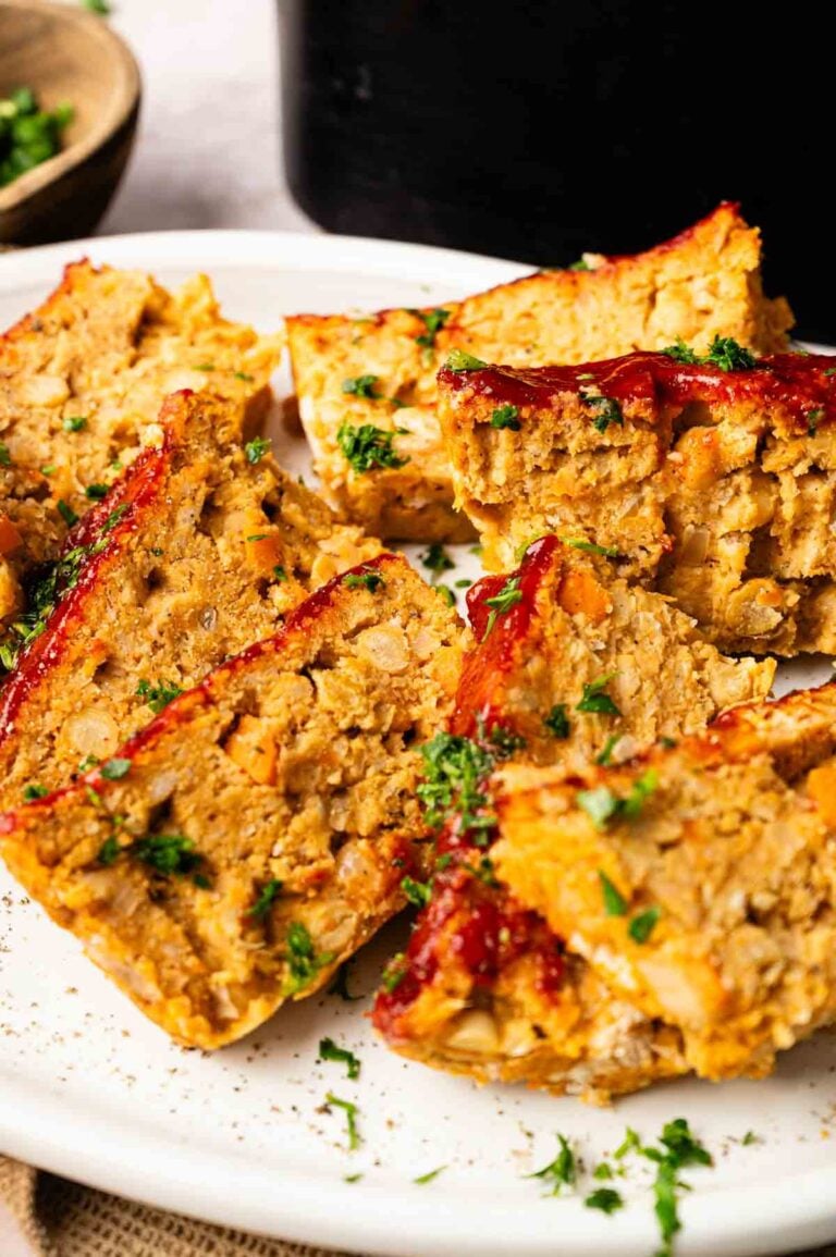 Several slices of Air Fryer Vegetarian Meatloaf topped with ketchup and chopped parsley are arranged on a white plate.