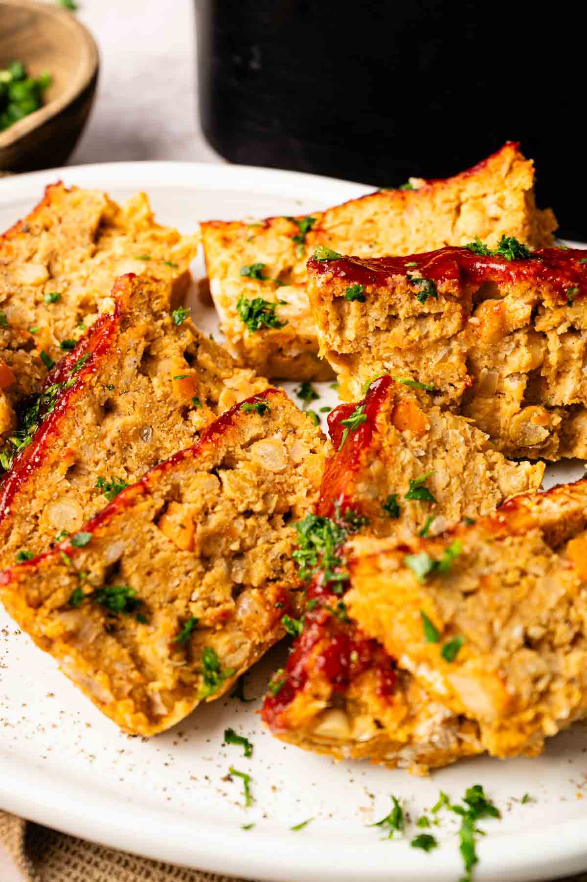 Several slices of Air Fryer Vegetarian Meatloaf topped with ketchup and chopped parsley are arranged on a white plate.