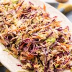 A plate of classic coleslaw made with shredded green and purple cabbage, crisp carrots, and tangy dressing, served on a white platter.