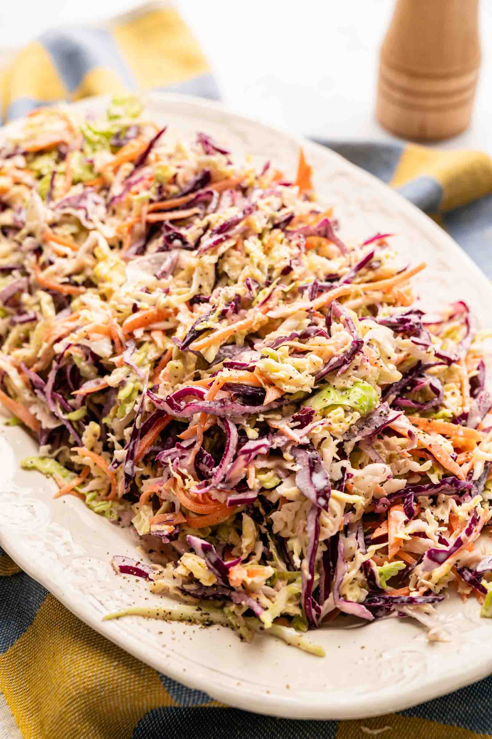 A plate of classic coleslaw made with shredded green and purple cabbage, crisp carrots, and tangy dressing, served on a white platter.