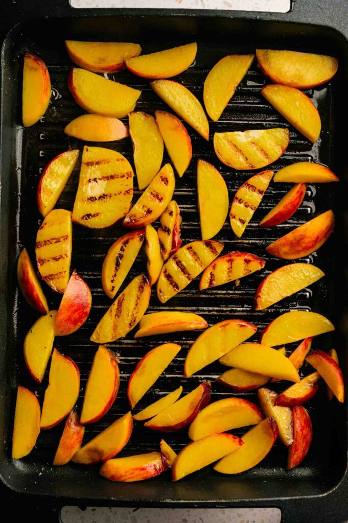 Grilled peaches with visible char marks are arranged on a black grill pan.