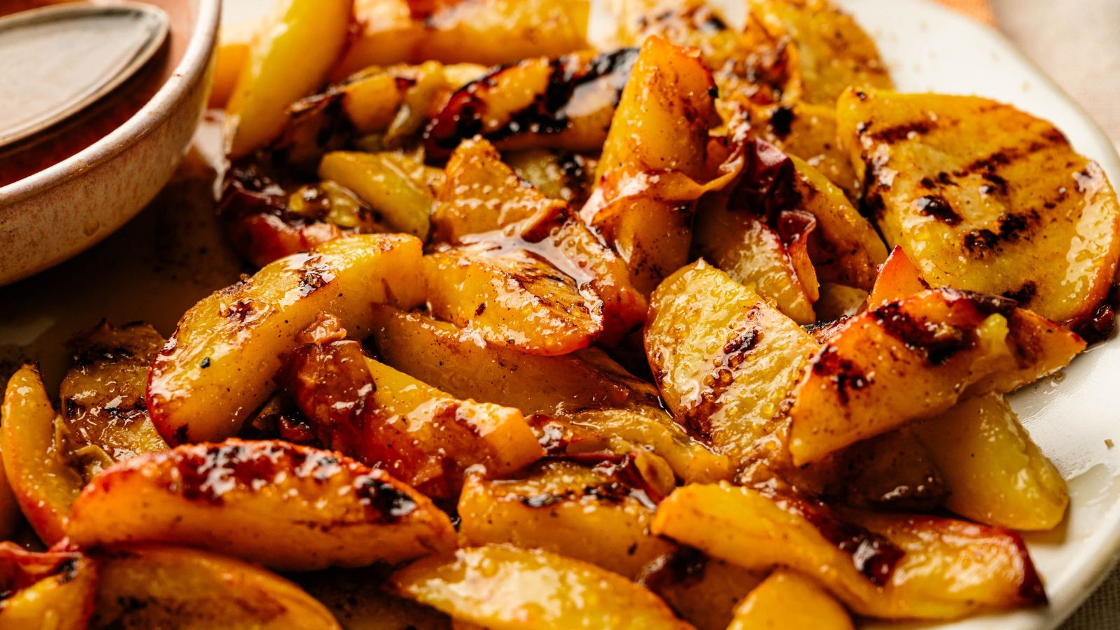 Close-up of grilled peach slices with caramelized, slightly charred edges on a white plate.