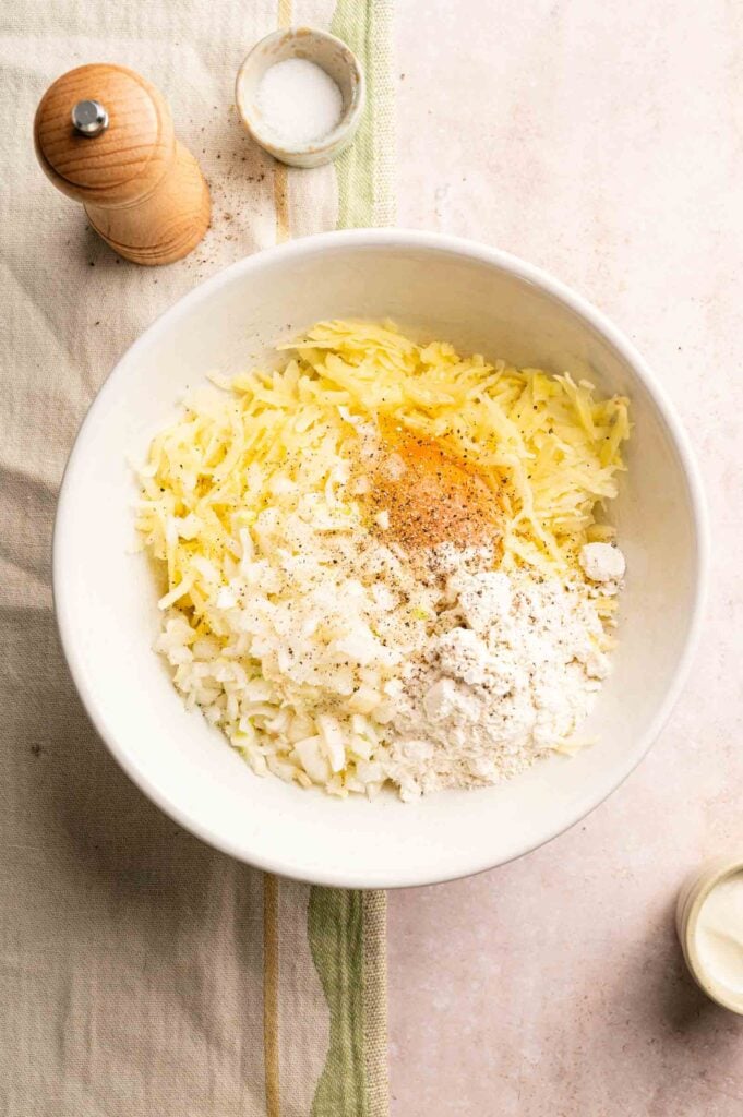 Shredded potatoes with other ingredients in a bowl for the potato fritters mixture.