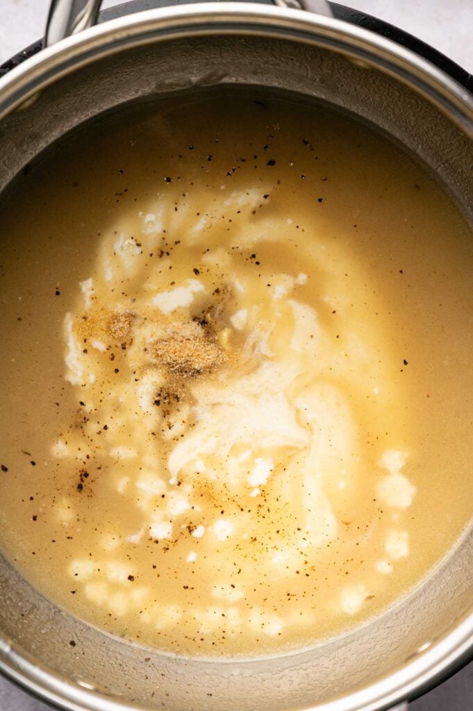 A pot of creamy soup being cooked, with visible swirls of cream, black pepper, and seasoning on the surface—perfect to pair with Air Fryer Vegetarian Meatballs for a comforting meal.