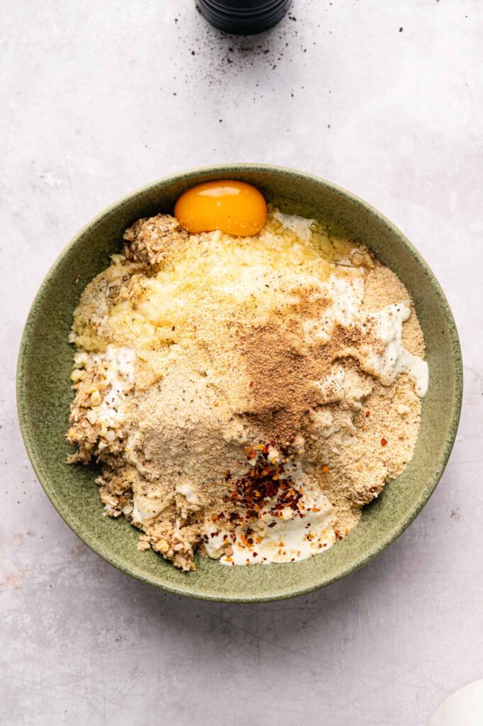 A green bowl containing ingredients like egg yolk, breadcrumbs, spices, and grated cheese—perfect for mixing Air Fryer Vegetarian Meatballs.