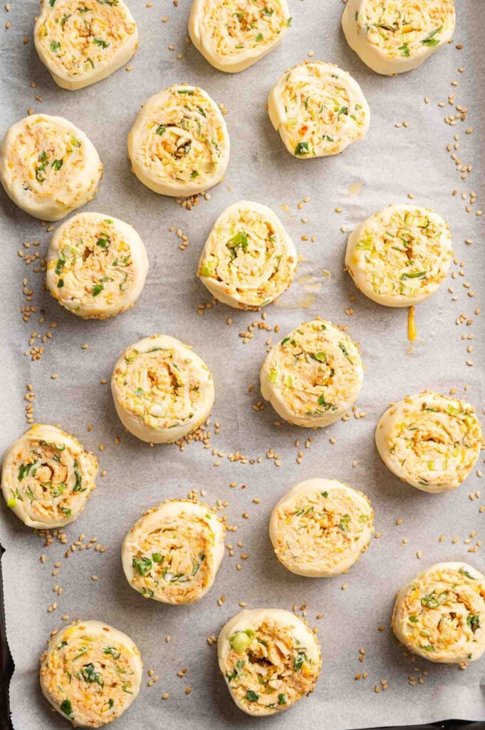 Unbaked savory vegetarian sausage roll filled with herbs, cheese, and flavors reminiscent of Vegetarian Sausage Rolls are arranged on a parchment-lined baking sheet, ready to be baked.