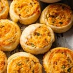 Golden-brown Vegetarian Sausage Rolls and cheese and herb puff pastry pinwheels are arranged on a baking sheet, showing flaky layers and melted cheese.
