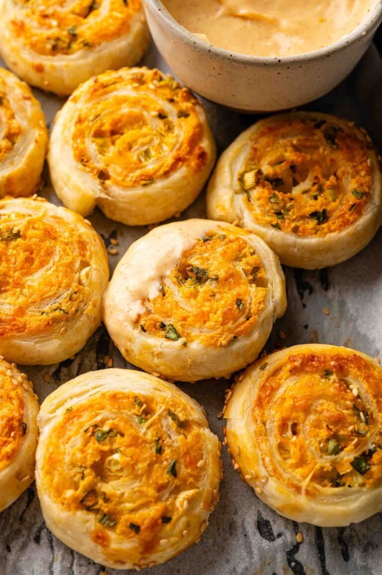 Golden-brown Vegetarian Sausage Rolls and cheese and herb puff pastry pinwheels are arranged on a baking sheet, showing flaky layers and melted cheese.
